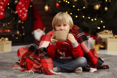 Photo of Little child with cup of hot drink on floor at home. Christmas celebration