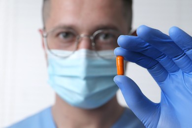 Doctor holding pill on light background, selective focus. Space for text