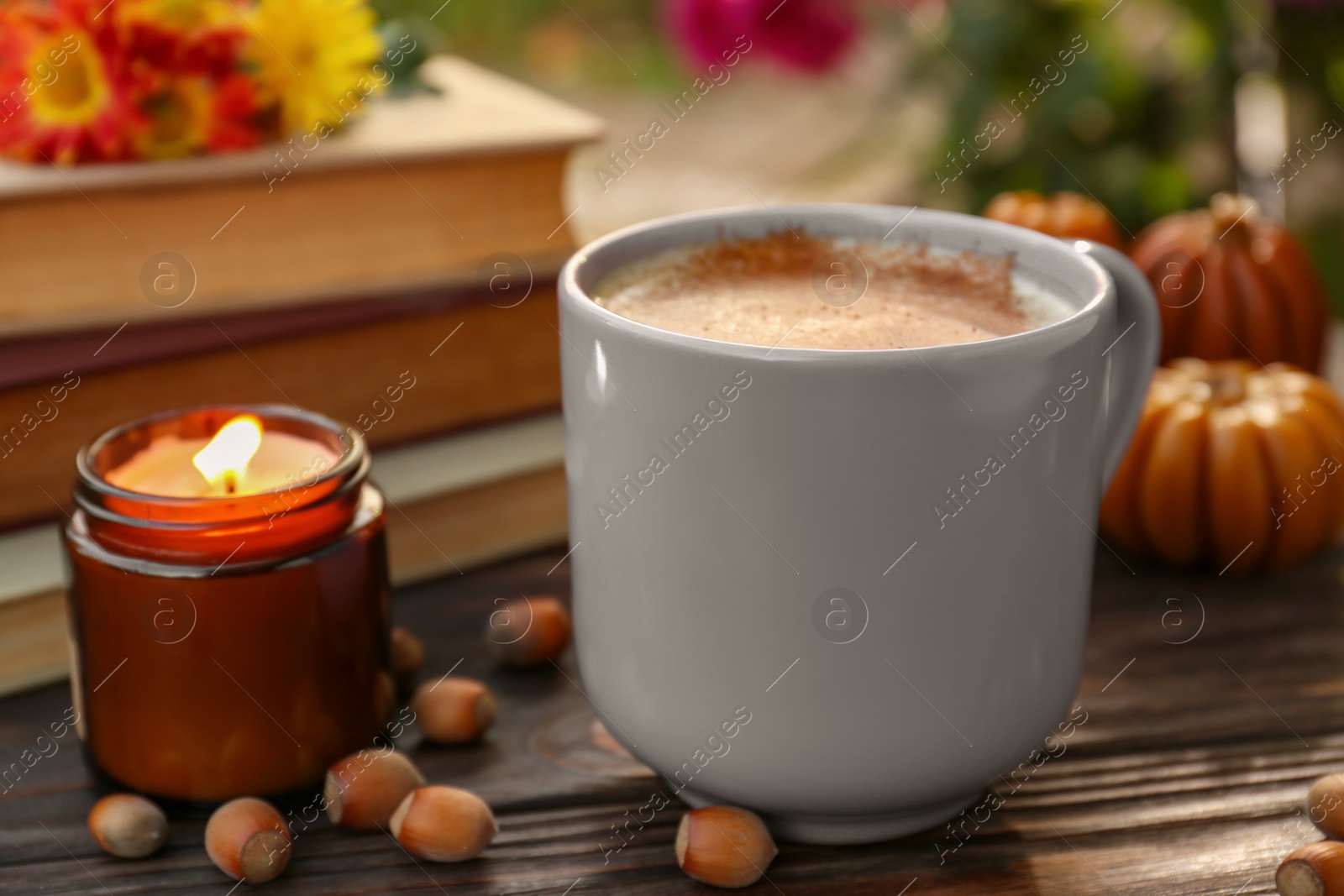 Photo of Cup of hot drink and burning candle on wooden table outdoors, closeup. Cozy autumn