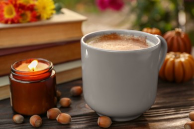 Cup of hot drink and burning candle on wooden table outdoors, closeup. Cozy autumn