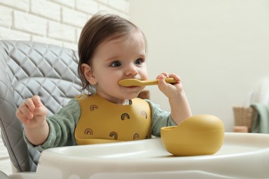 Cute little baby eating healthy food in high chair indoors