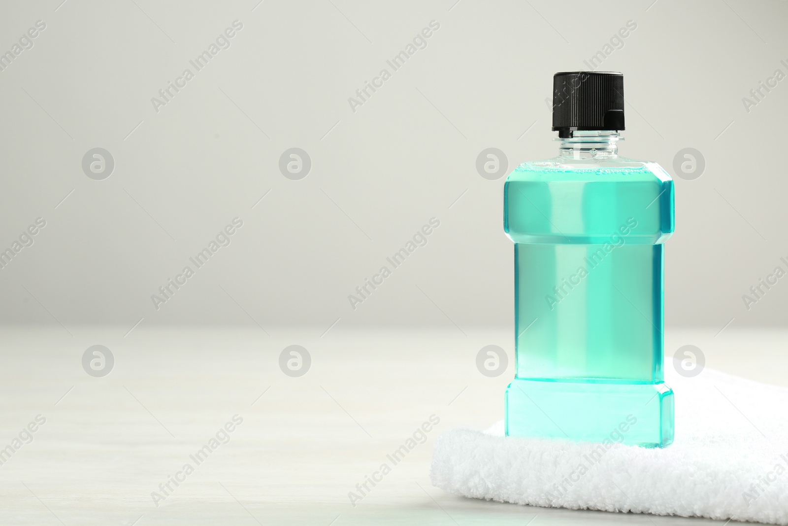 Photo of Mouthwash with towel and space for text on light background. Teeth hygiene