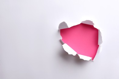 Hole in white paper on pink background, space for text