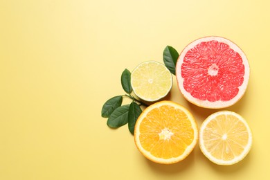 Photo of Different cut citrus fruits and leaves on yellow table, flat lay. Space for text