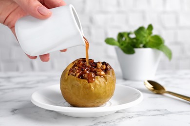 Woman pouring caramel onto delicious baked apple on white marble table, closeup