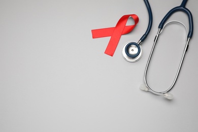 Photo of Red ribbon and stethoscope on light grey background, flat lay with space for text. AIDS disease awareness