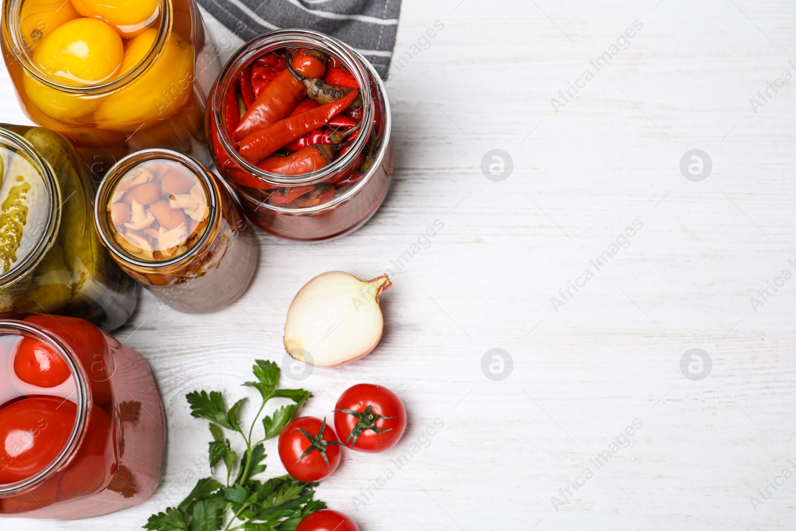 Photo of Glass jars with different pickled vegetables on white wooden table, flat lay. Space for text