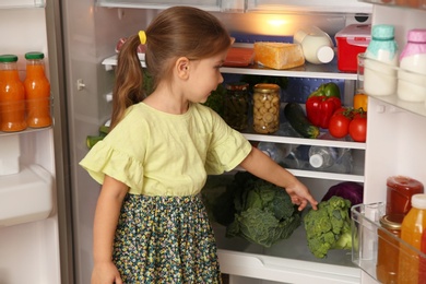 Cute little girl choosing food in refrigerator at home