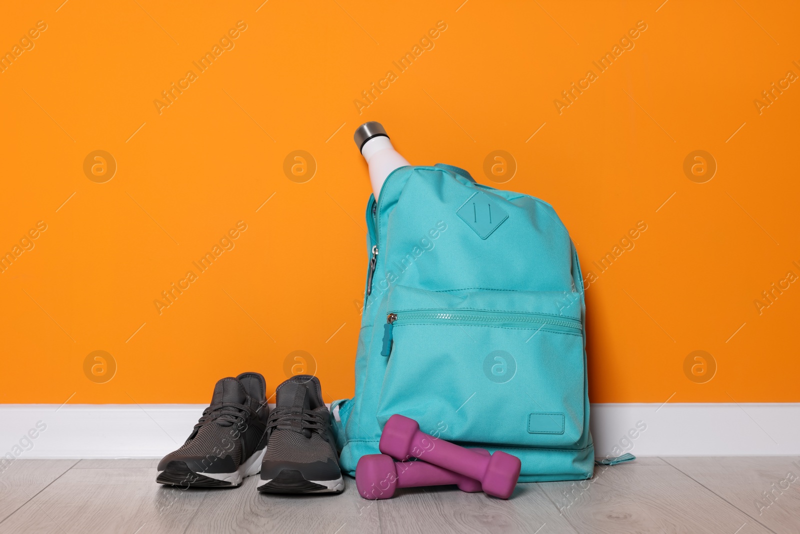 Photo of Backpack and sports equipment on floor near orange wall