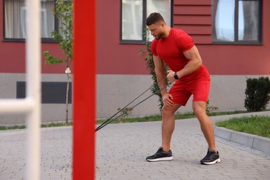 Photo of Muscular man doing exercise with elastic resistance band on sports ground