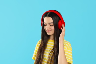 Photo of Teenage girl listening music with headphones on light blue background. Space for text