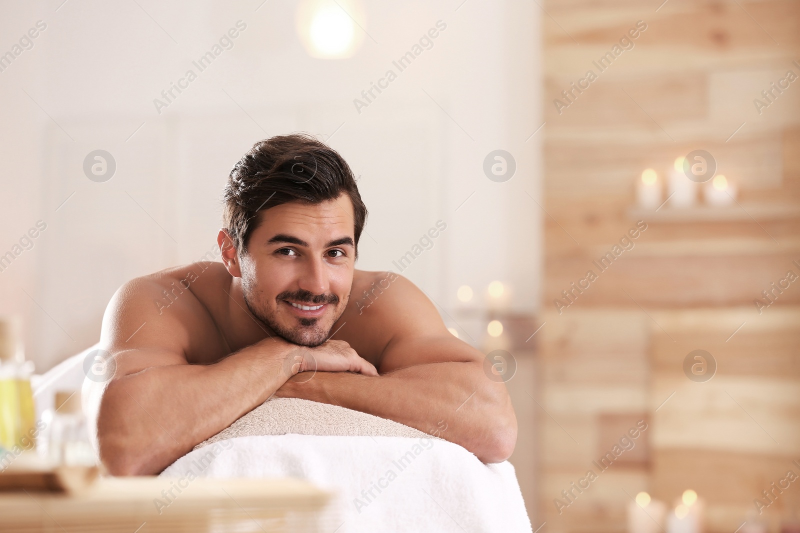 Photo of Handsome young man relaxing on massage table in spa salon, space for text