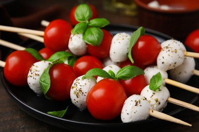 Photo of Delicious Caprese skewers with tomatoes, mozzarella balls, basil and spices on table, closeup