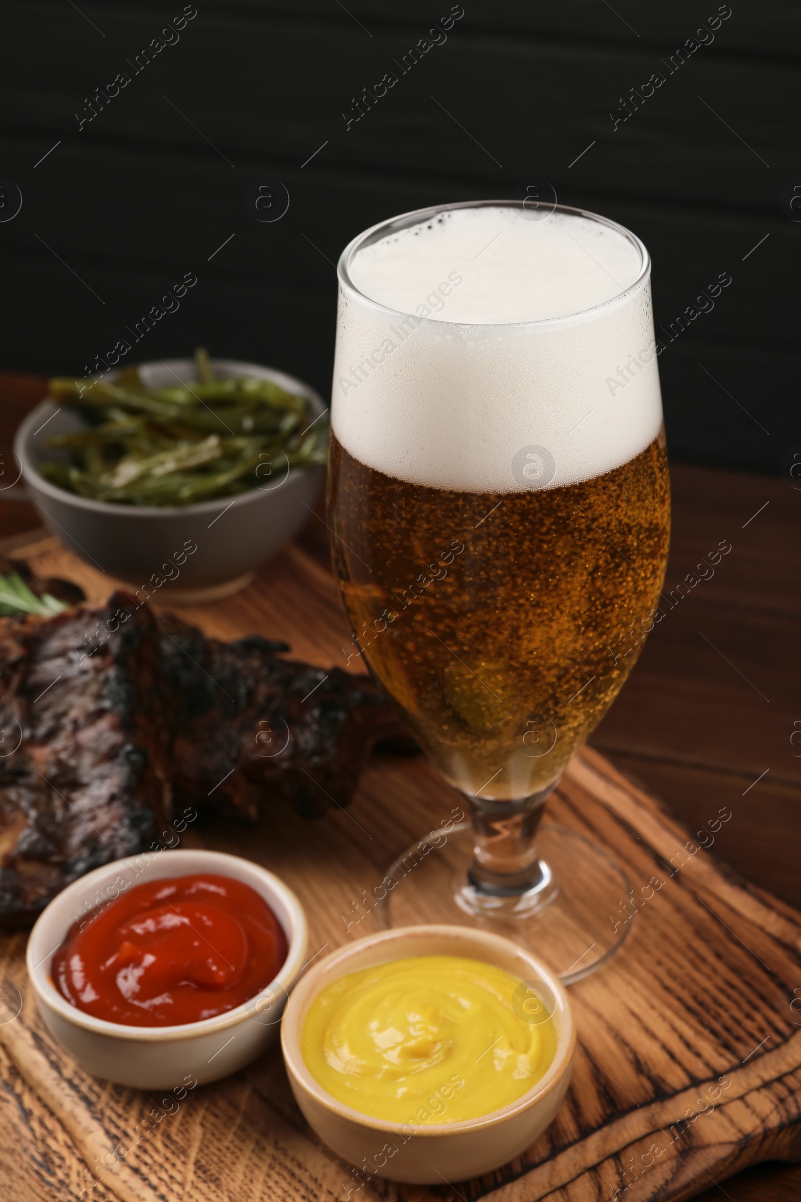 Photo of Glass of beer, delicious grilled ribs and sauces on wooden table