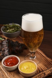 Glass of beer, delicious grilled ribs and sauces on wooden table