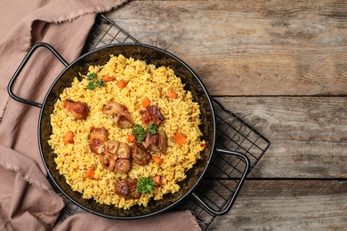 Photo of Frying pan of delicious rice pilaf and napkin on wooden background, top view with space for text