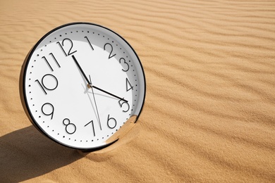 Stylish clock on sand in desert. Space for text