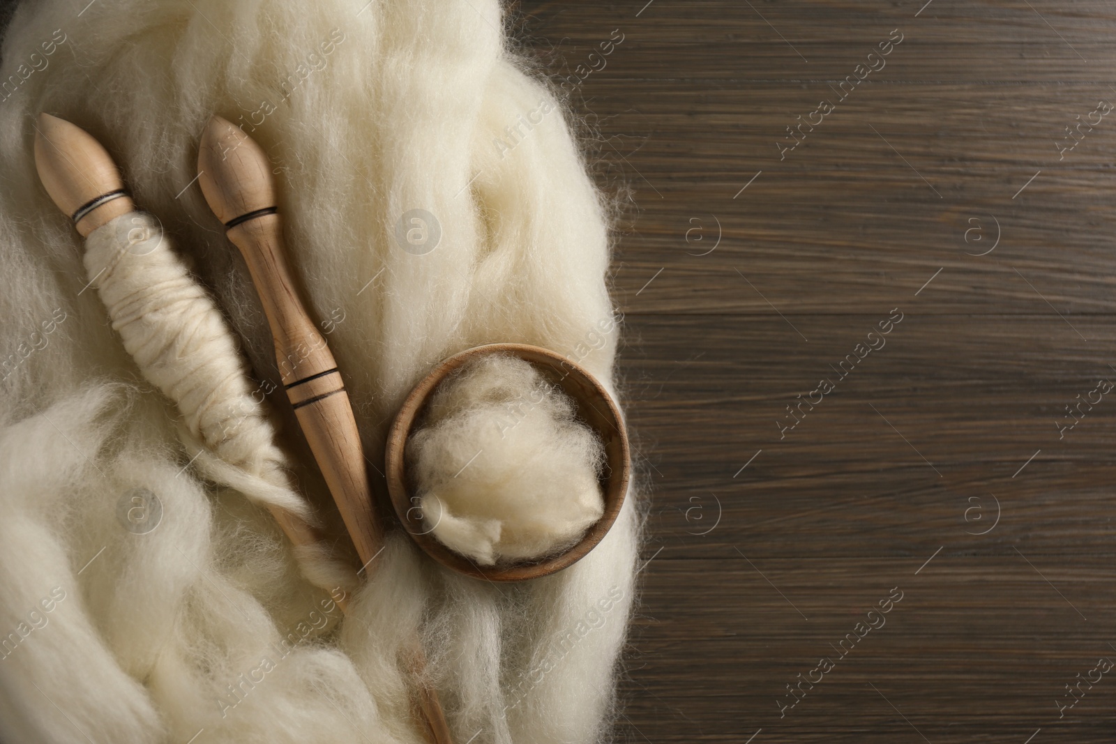 Photo of Soft white wool and spindles on wooden table, flat lay. Space for text