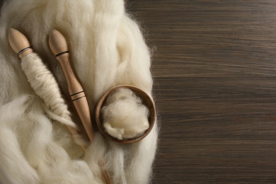 Soft white wool and spindles on wooden table, flat lay. Space for text