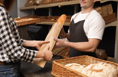 Woman buying fresh baguette in bakery shop, closeup