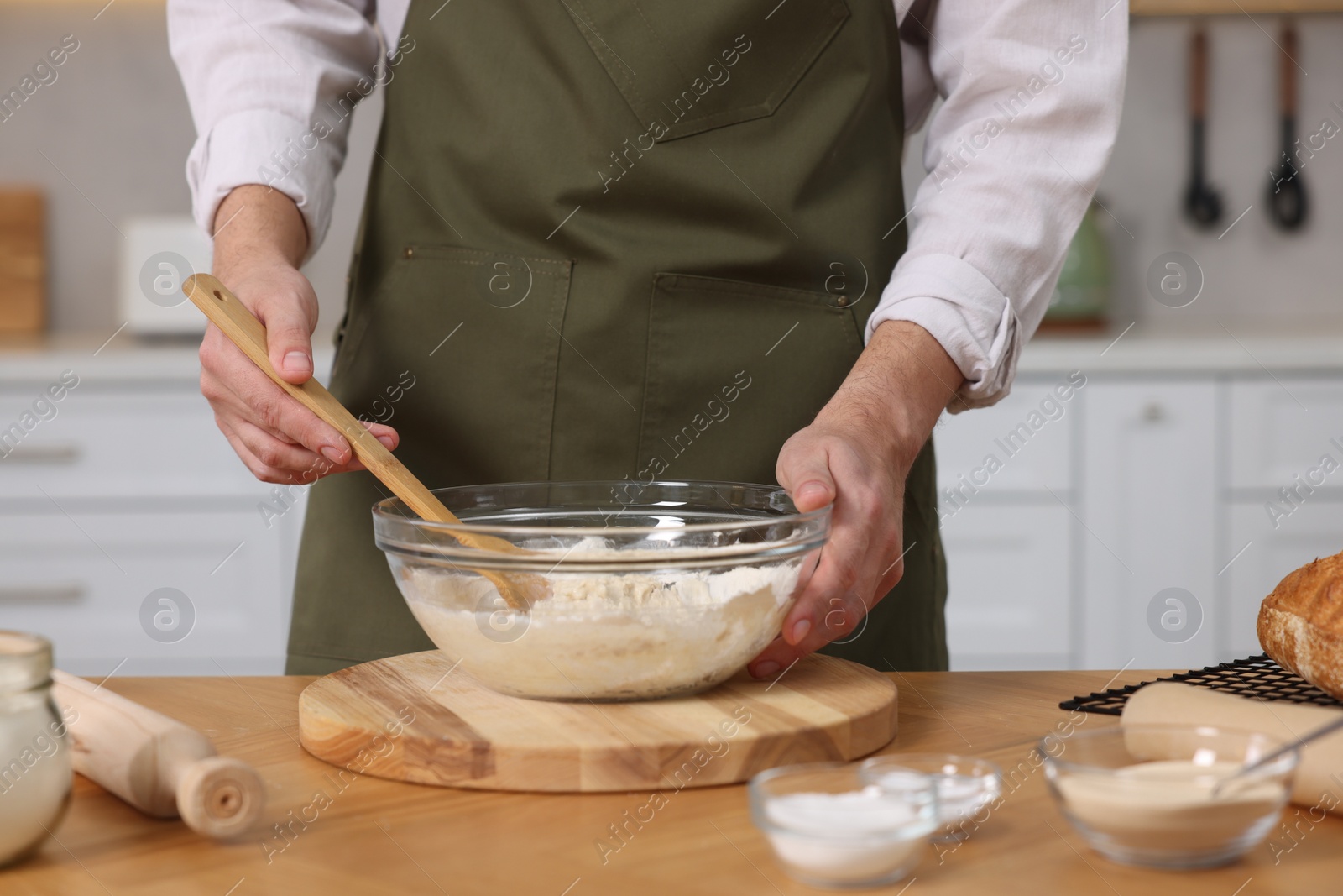 Photo of Making bread. Man preparing dough in bowl at wooden table in kitchen, closeup