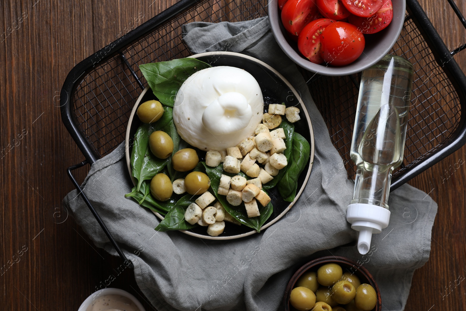 Photo of Delicious burrata cheese served with olives, croutons, basil and tomatoes on wooden table, top view