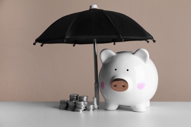 Photo of Small umbrella and piggy bank with coins on white table