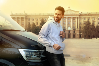 Image of Handsome young man near modern car outdoors