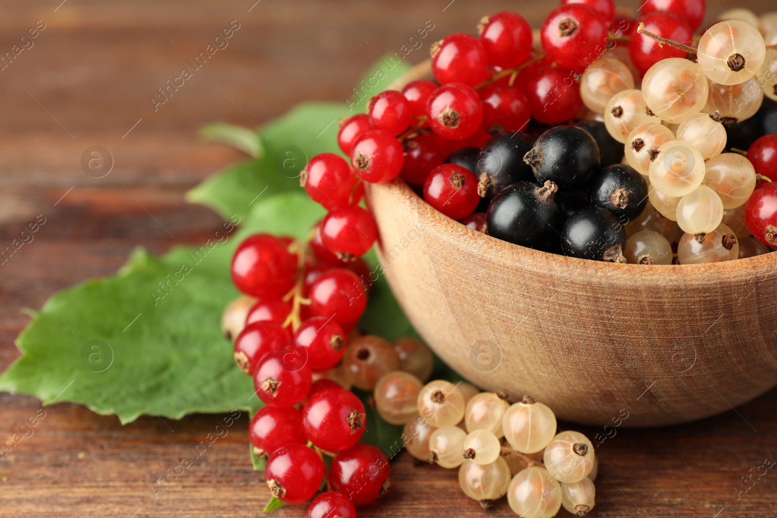 Photo of Different fresh ripe currants and green leaves on wooden table, closeup