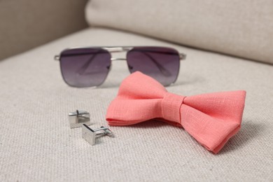 Photo of Stylish pink bow tie, sunglasses and cufflinks on light grey sofa, closeup
