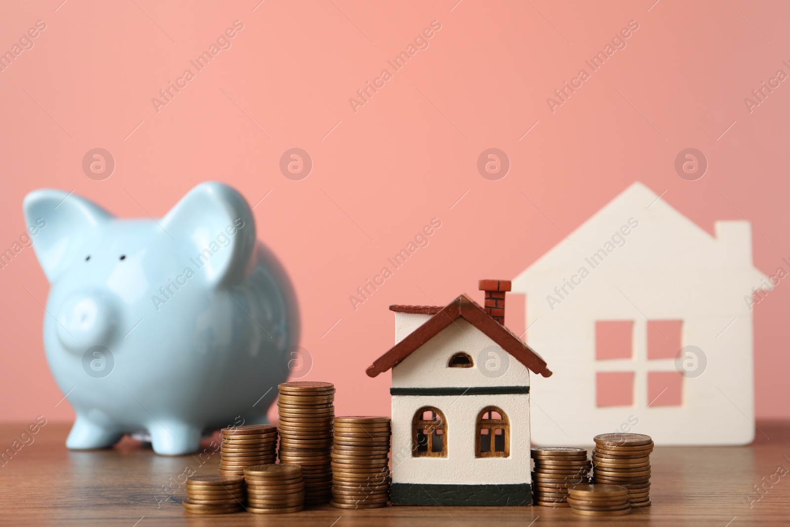 Photo of House models, piggy bank and stacked coins on wooden table against pink background, selective focus