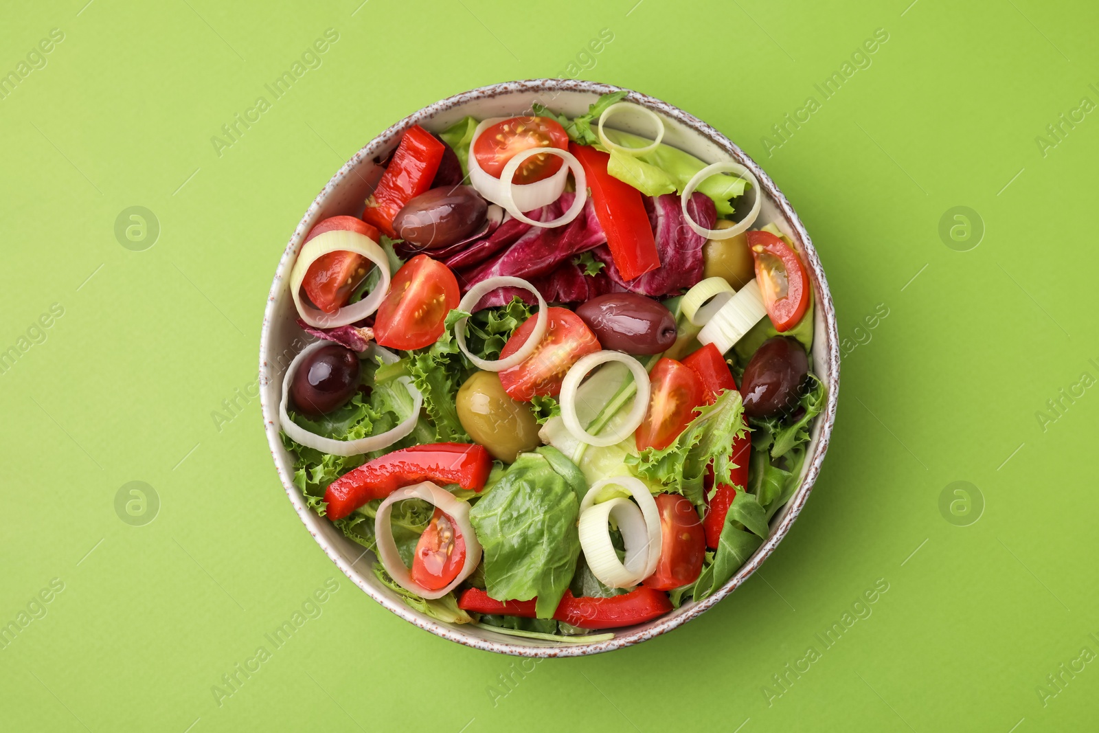 Photo of Bowl of tasty salad with leek and olives on light green table, top view
