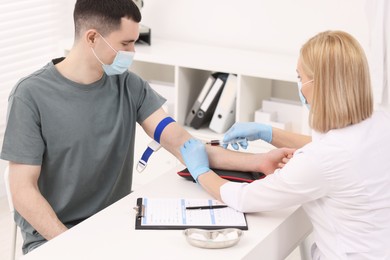 Doctor taking blood sample from patient with syringe at white table in hospital