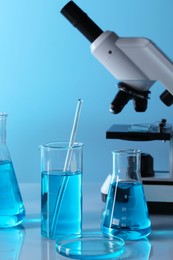 Different laboratory glassware with light blue liquid and microscope on table