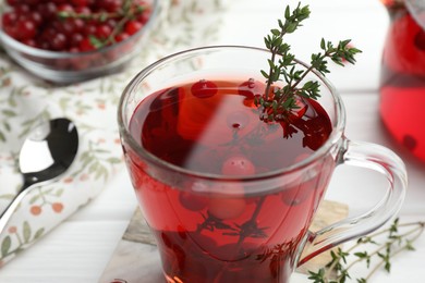 Photo of Tasty hot cranberry tea with thyme and fresh berries in glass cup on white table