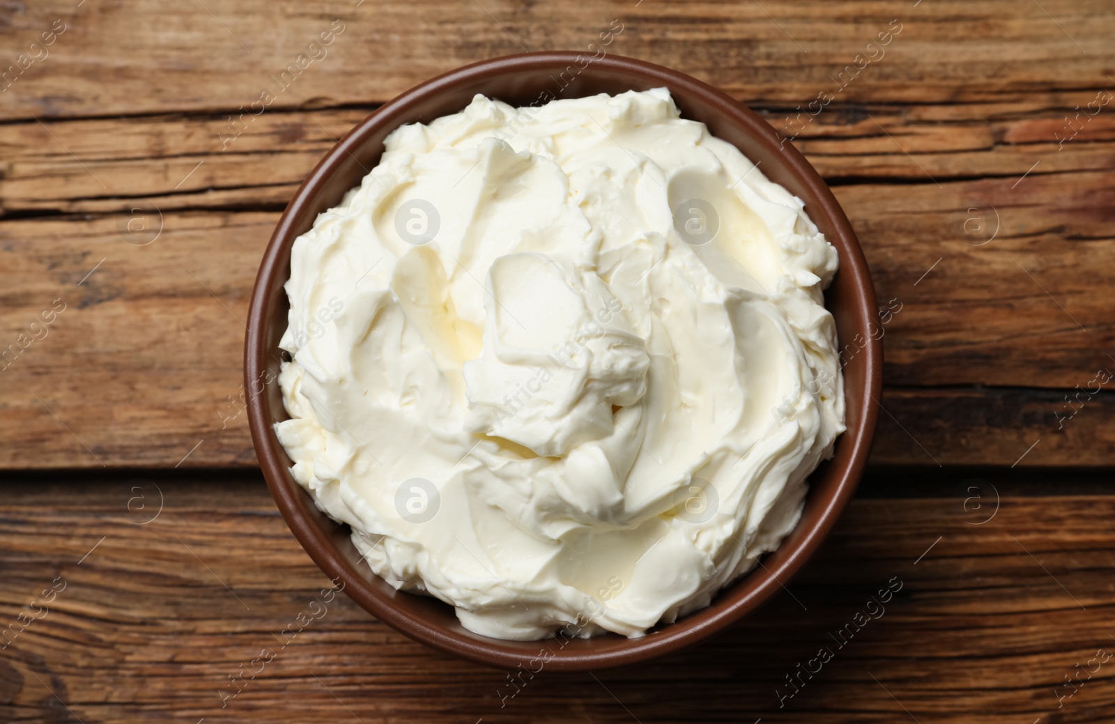 Photo of Bowl of tasty cream cheese on wooden table, top view