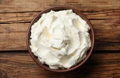 Bowl of tasty cream cheese on wooden table, top view