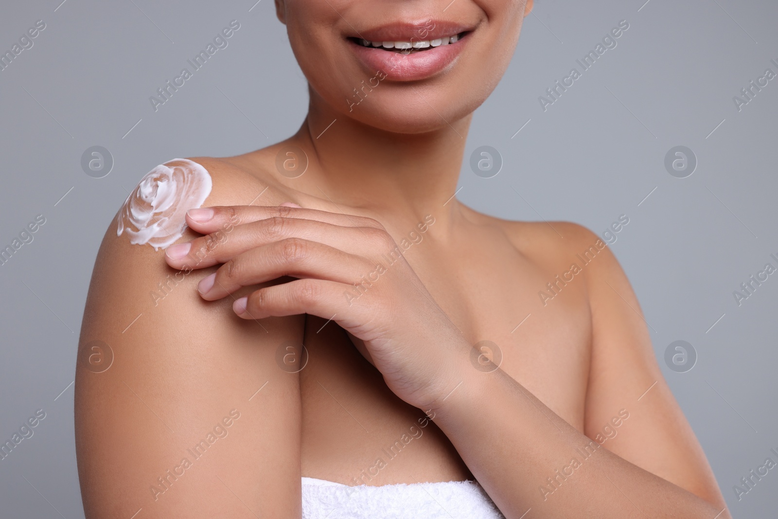 Photo of Young woman applying body cream onto shoulder on grey background, closeup