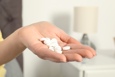 Woman holding many pills in hand indoors, closeup view