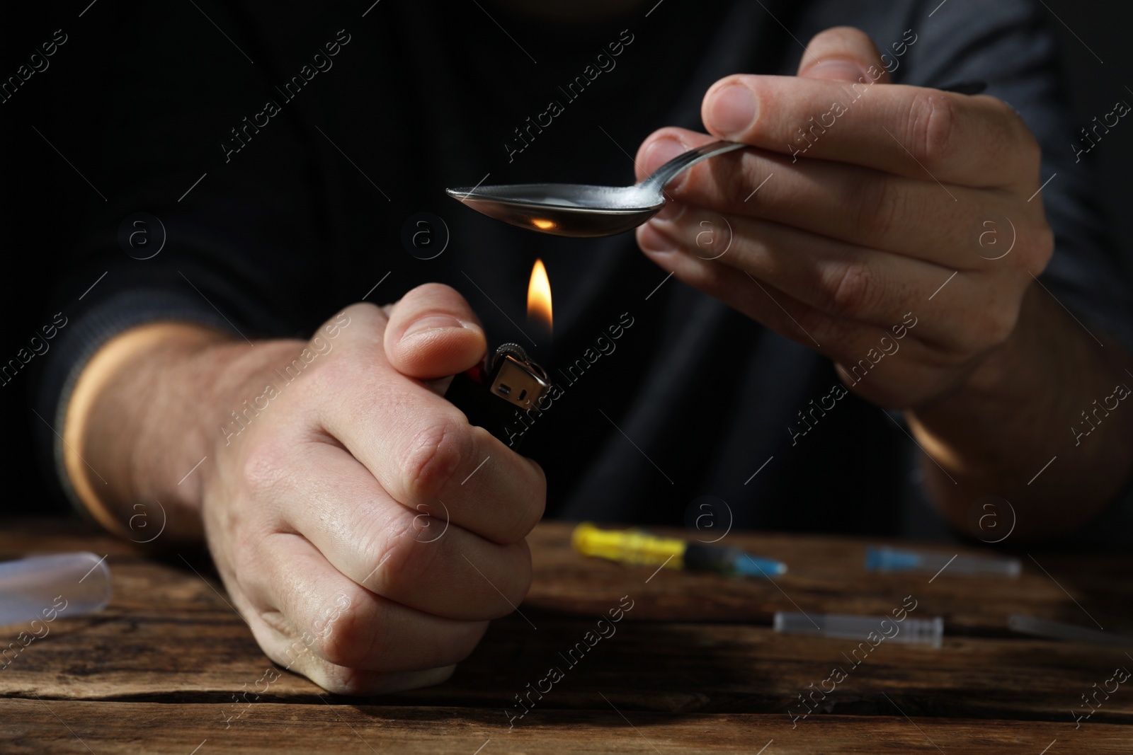 Photo of Man preparing drugs with spoon and lighter at wooden table, closeup