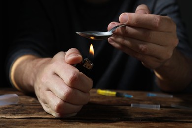 Man preparing drugs with spoon and lighter at wooden table, closeup