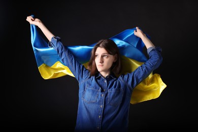 Young woman holding Ukrainian flag on black background