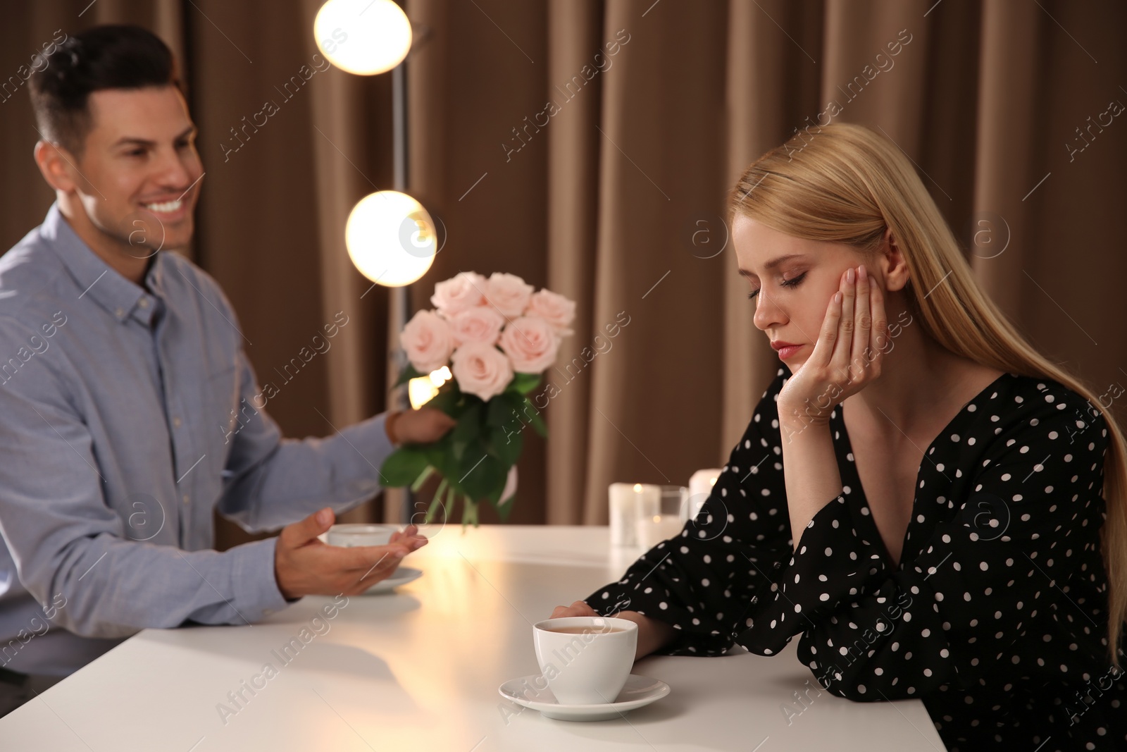 Photo of Man giving flowers to displeased young woman in restaurant. Failed first date