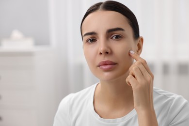 Photo of Woman with dry skin checking her face indoors, space for text