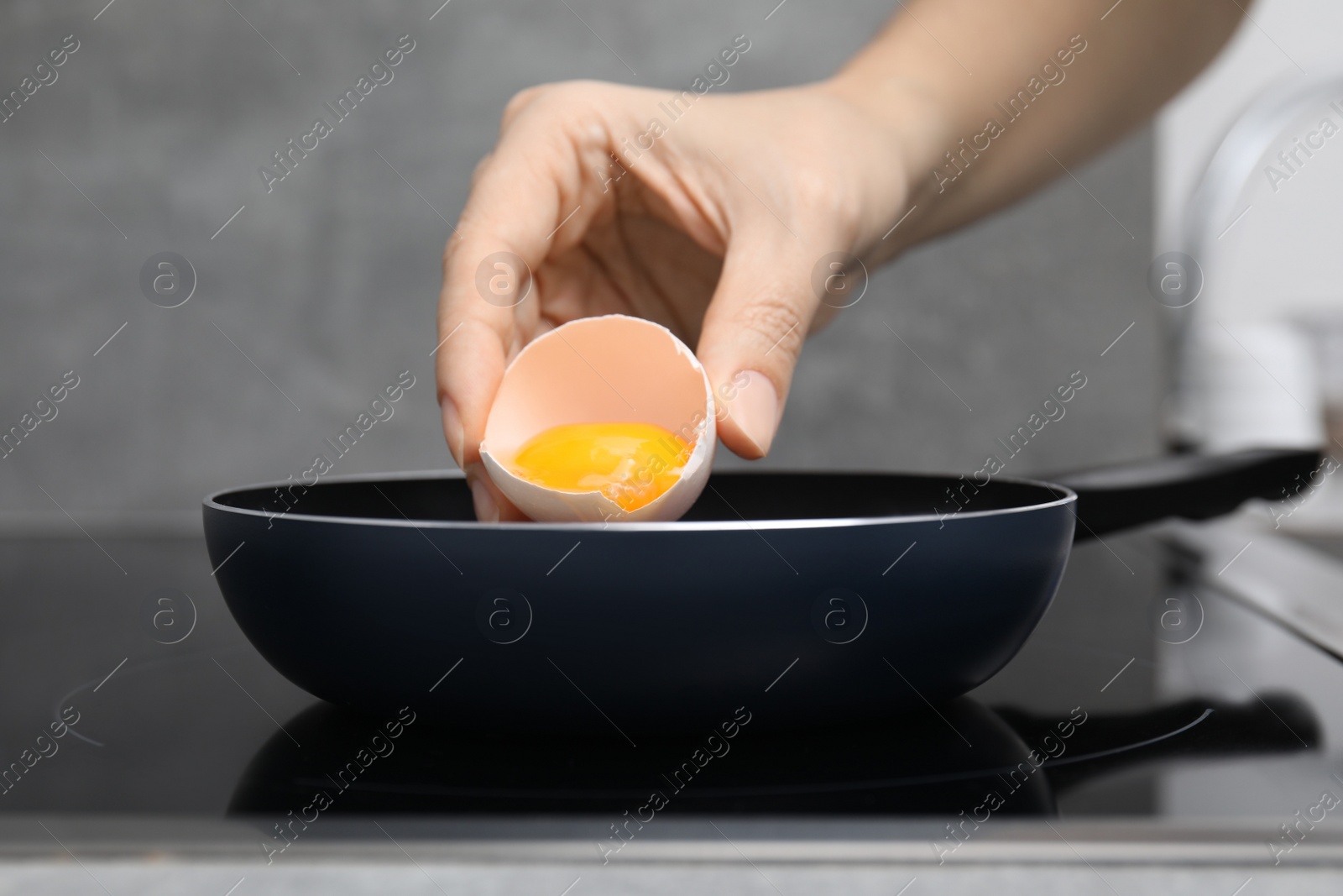 Photo of Woman breaking egg into frying pan, closeup