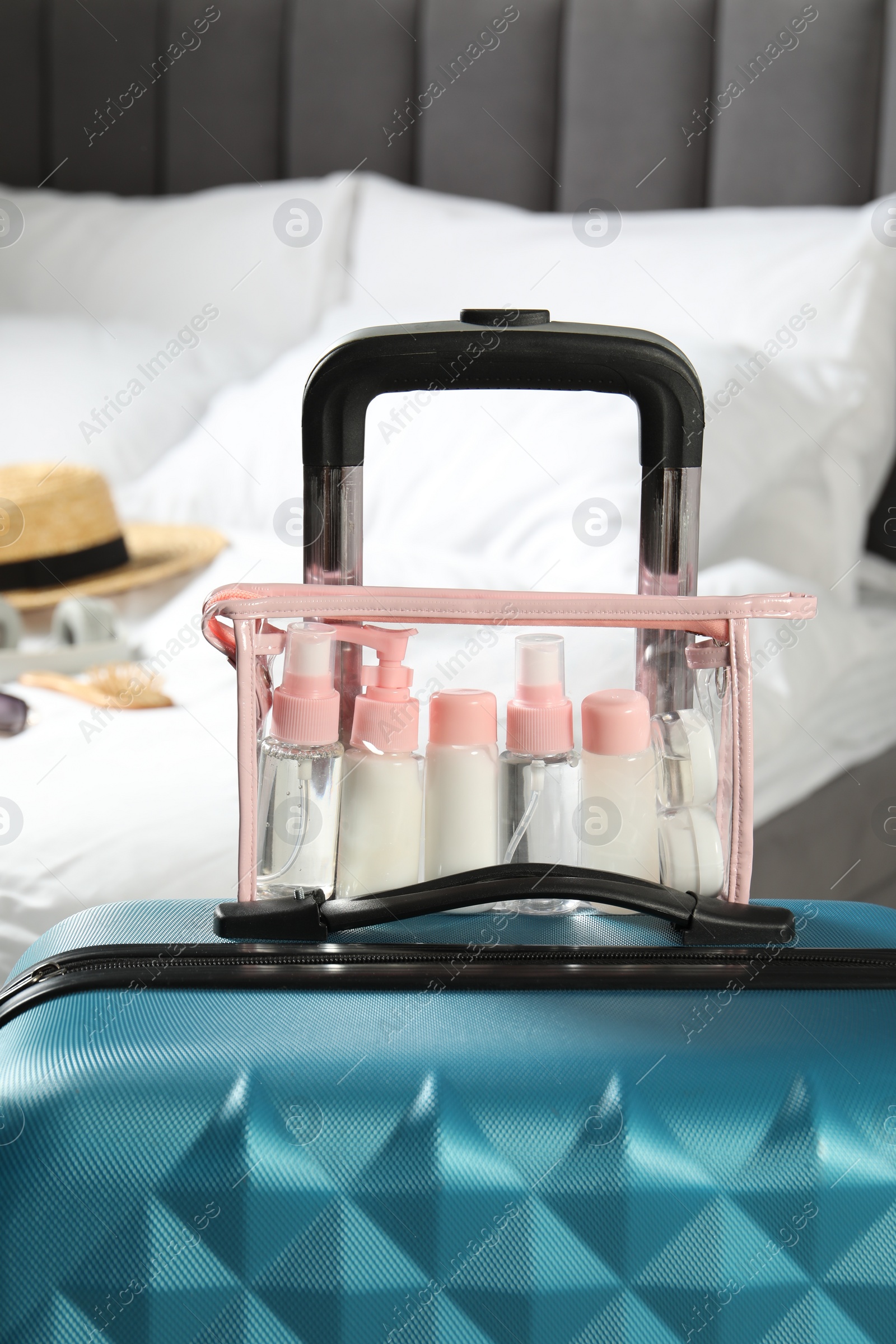 Photo of Cosmetic travel kit. Plastic bag with small containers of personal care products on suitcase in bedroom