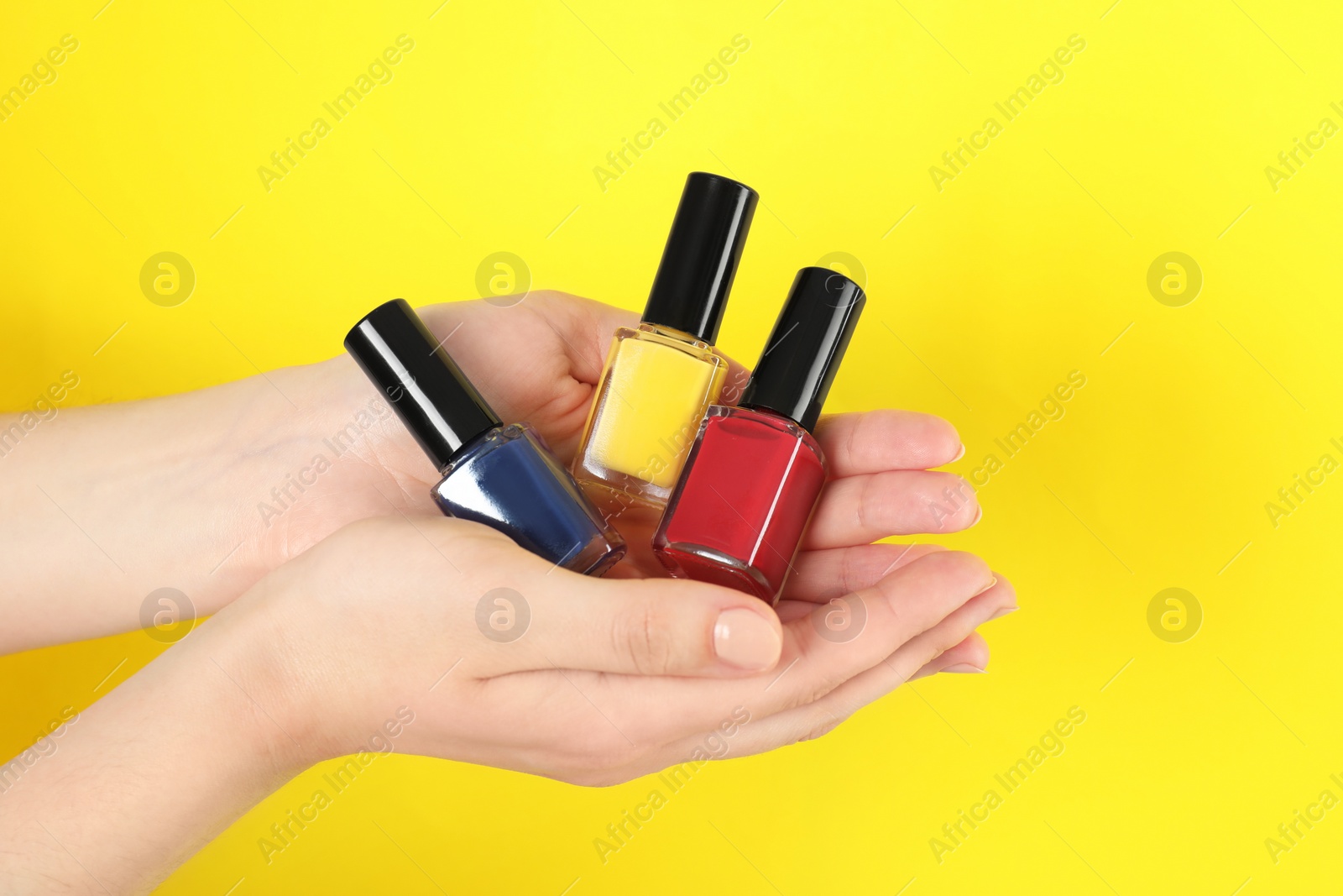 Photo of Woman holding nail polishes on yellow background, closeup