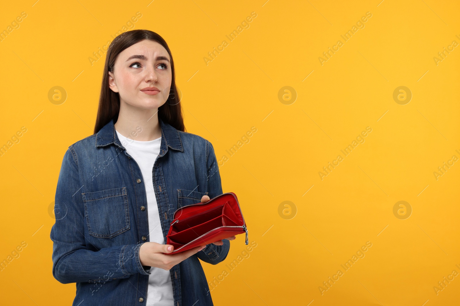 Photo of Sad woman showing empty wallet on orange background, space for text