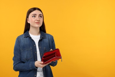 Sad woman showing empty wallet on orange background, space for text