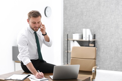 Photo of Young businessman talking by mobile phone in office, space for text